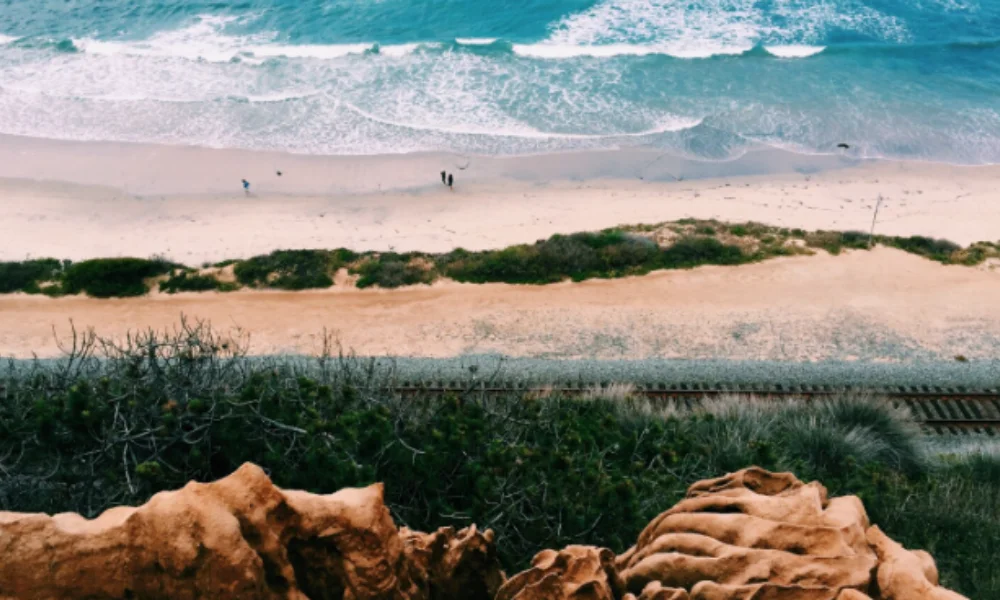 A scenic view from a cliff overlooking a beach with gentle waves