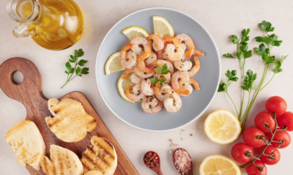 A plate of shrimp with lemon slices and parsley on a gray dish sits beside grilled bread