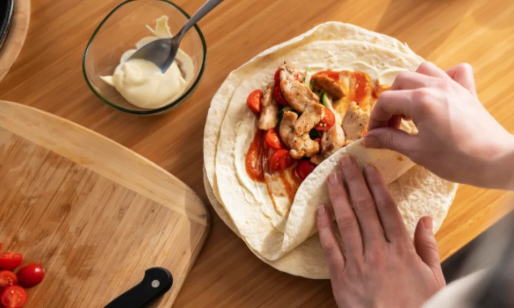 Hands are folding a tortilla filled with chicken, vegetables, and sauce-easy birria tacos recipe
