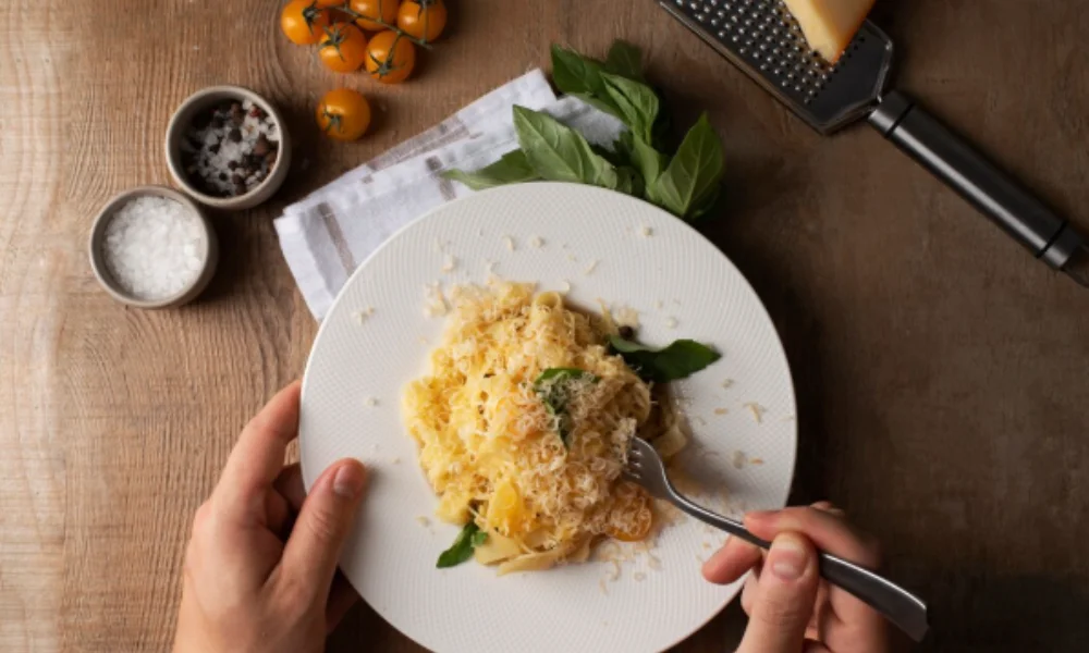 A person holds a fork over a white plate of pasta topped with grated cheese and basil-easy alfredo sauce recipe