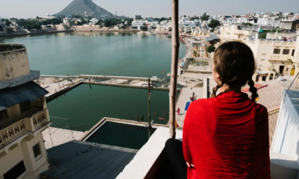 Woman in a red shirt with braided hair sits on a rooftop