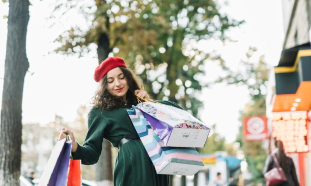 A woman in a red beret and green coat joyfully holds colorful shopping bags on a tree-lined street-washington dc travel guide