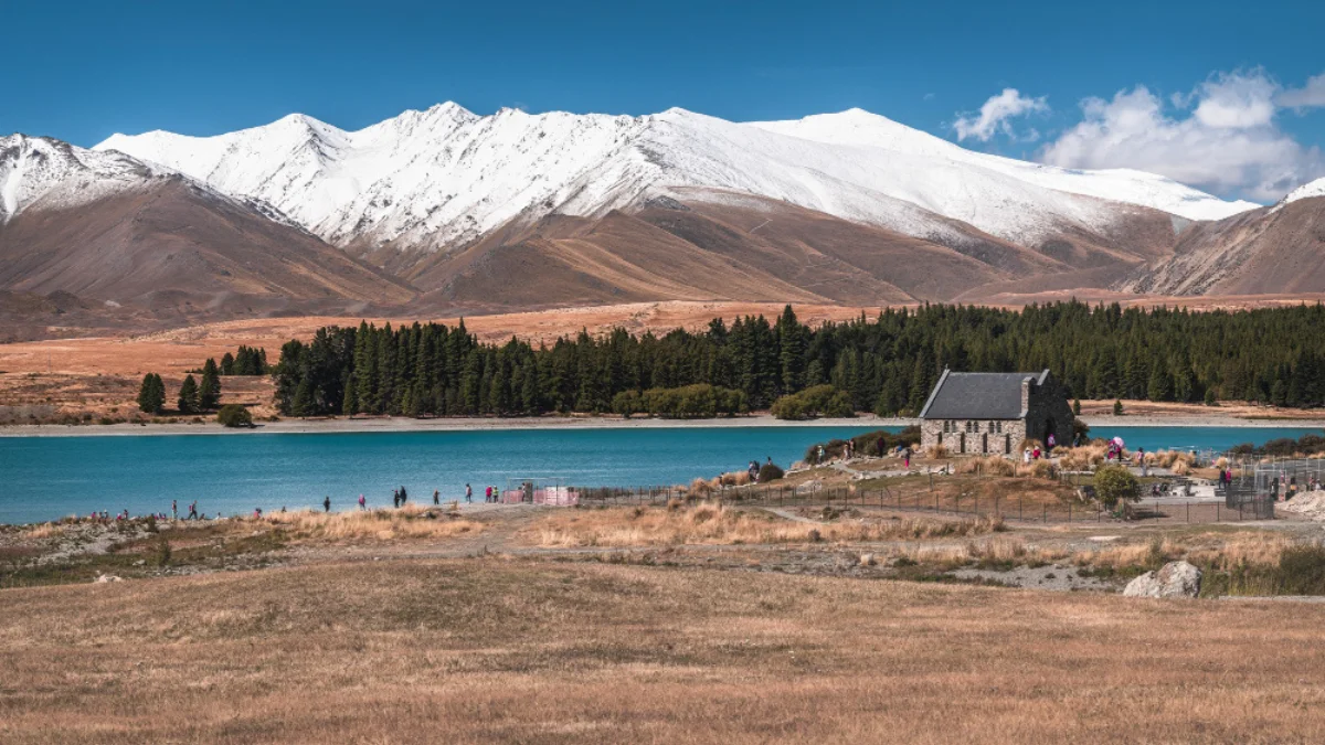 Scenic view of a lakeside chapel, surrounded by golden grass, clear blue water
