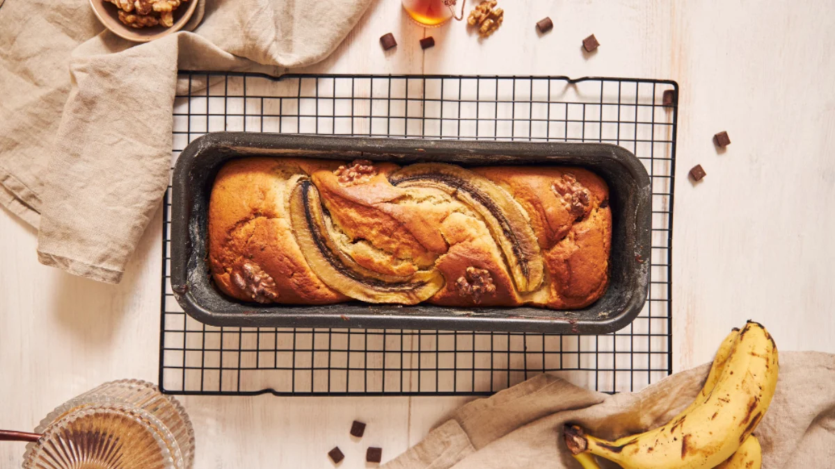 Banana bread in a loaf pan on a cooling rack.