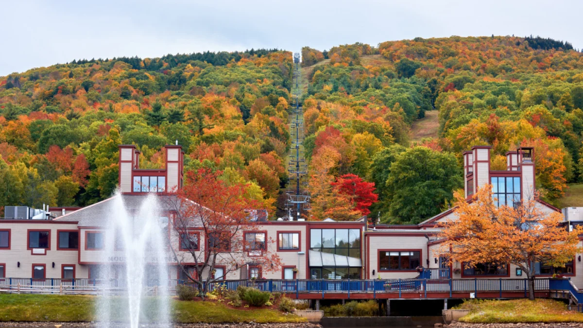 A lodge with large windows and red accents sits in front of a hillside covered in vibrant autumn foliage