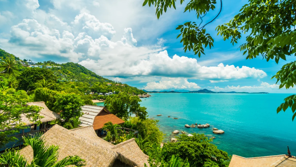 Tropical coastal scene with turquoise sea, lush greenery, and thatched-roof huts