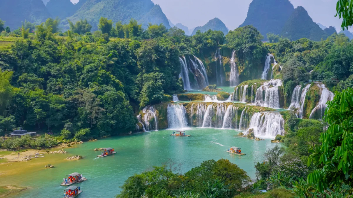 Lush green scenery surrounds a series of cascading waterfalls flowing into a turquoise river
