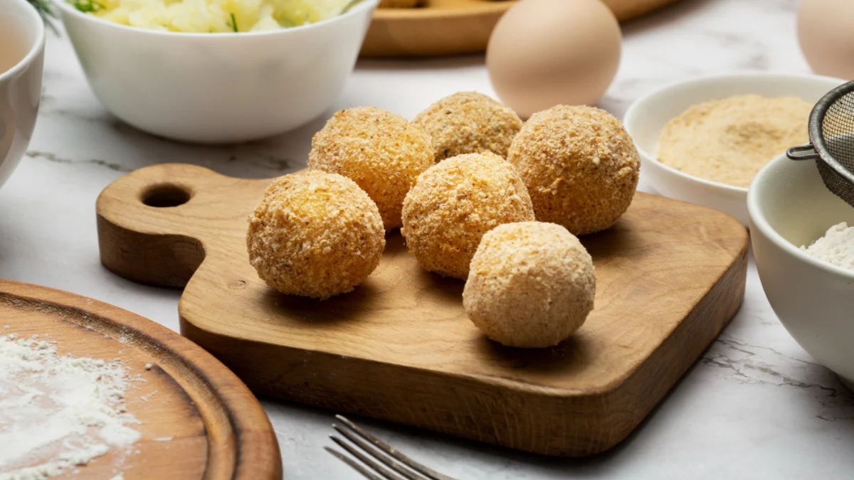 Golden brown croquettes on a wooden board, surrounded by ingredients like eggs
