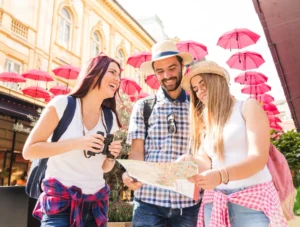 A cheerful group of three friends, two women and one man, standing outdoors under pink umbrellas
