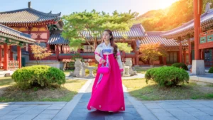 A woman in a vibrant pink hanbok stands in a traditional Korean courtyard