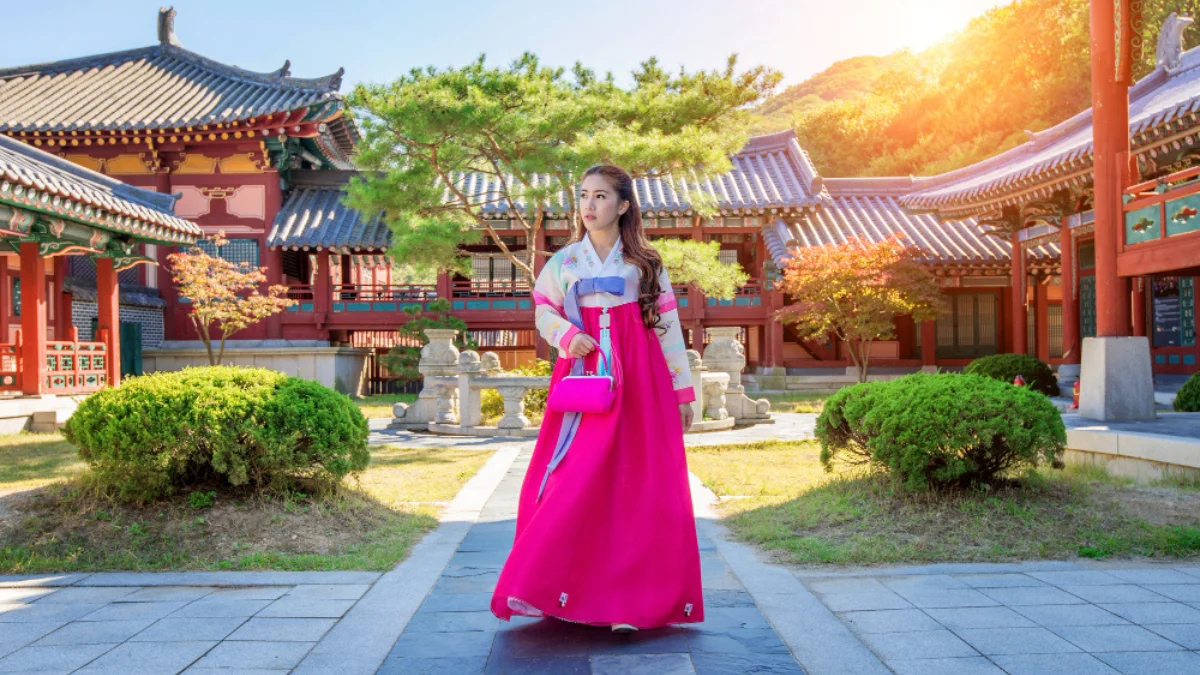 A woman in a vibrant pink hanbok stands in a traditional Korean courtyard