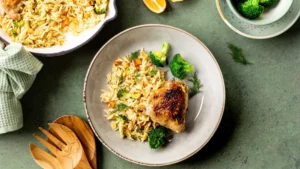 A plate of orzo with vegetables, topped with a crispy chicken thigh and garnished with dill