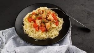 A black plate with spaghetti topped with chunky tomato sauce and herbs