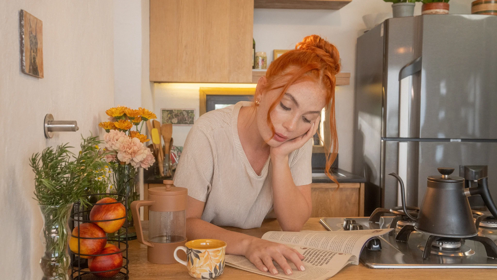 A woman sits in the kitchen, engrossed in reading a book, surrounded by warm, inviting decor.