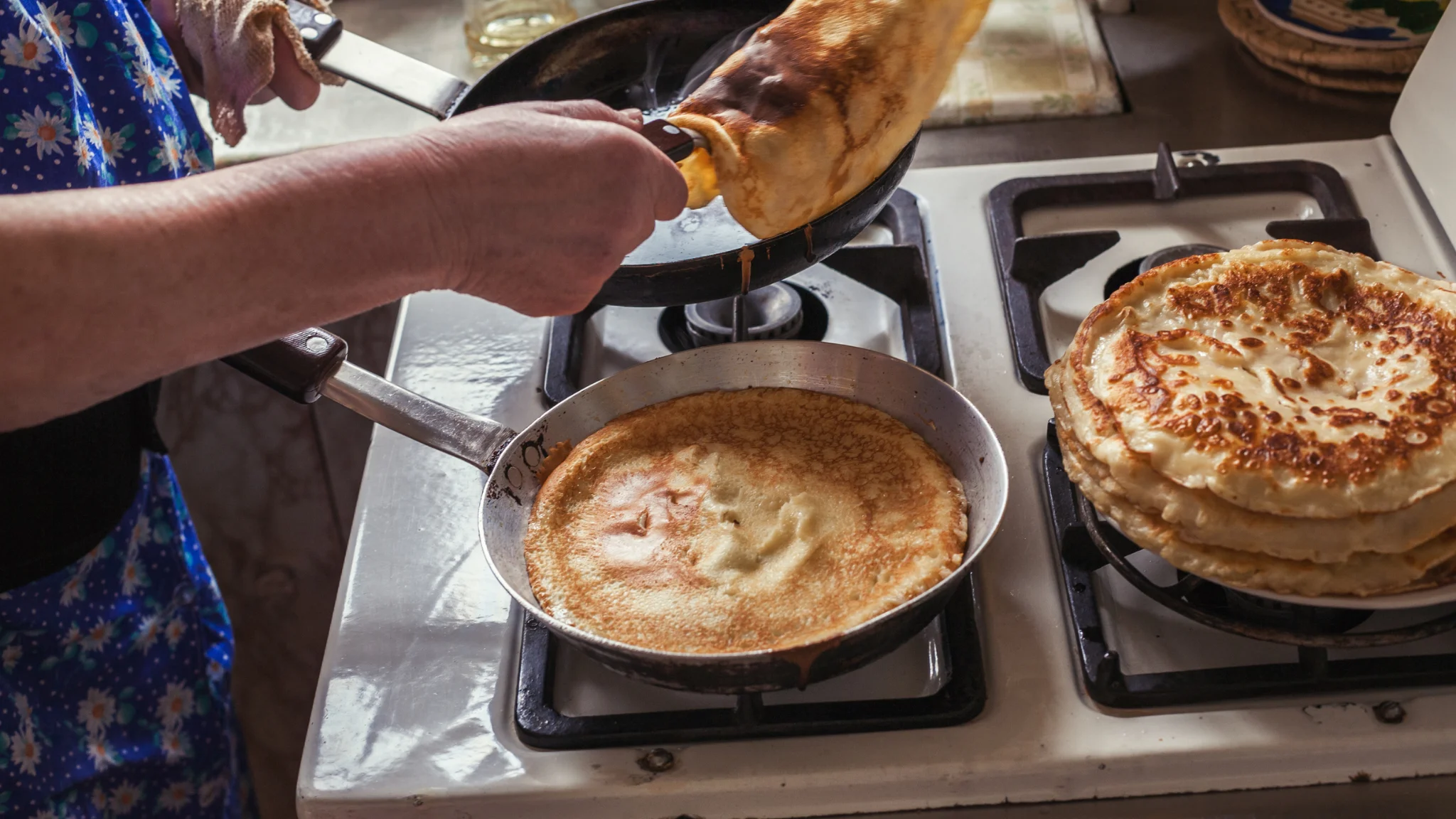 A person is cooking pancakes on a stove, flipping them with a spatula in a cozy kitchen setting.