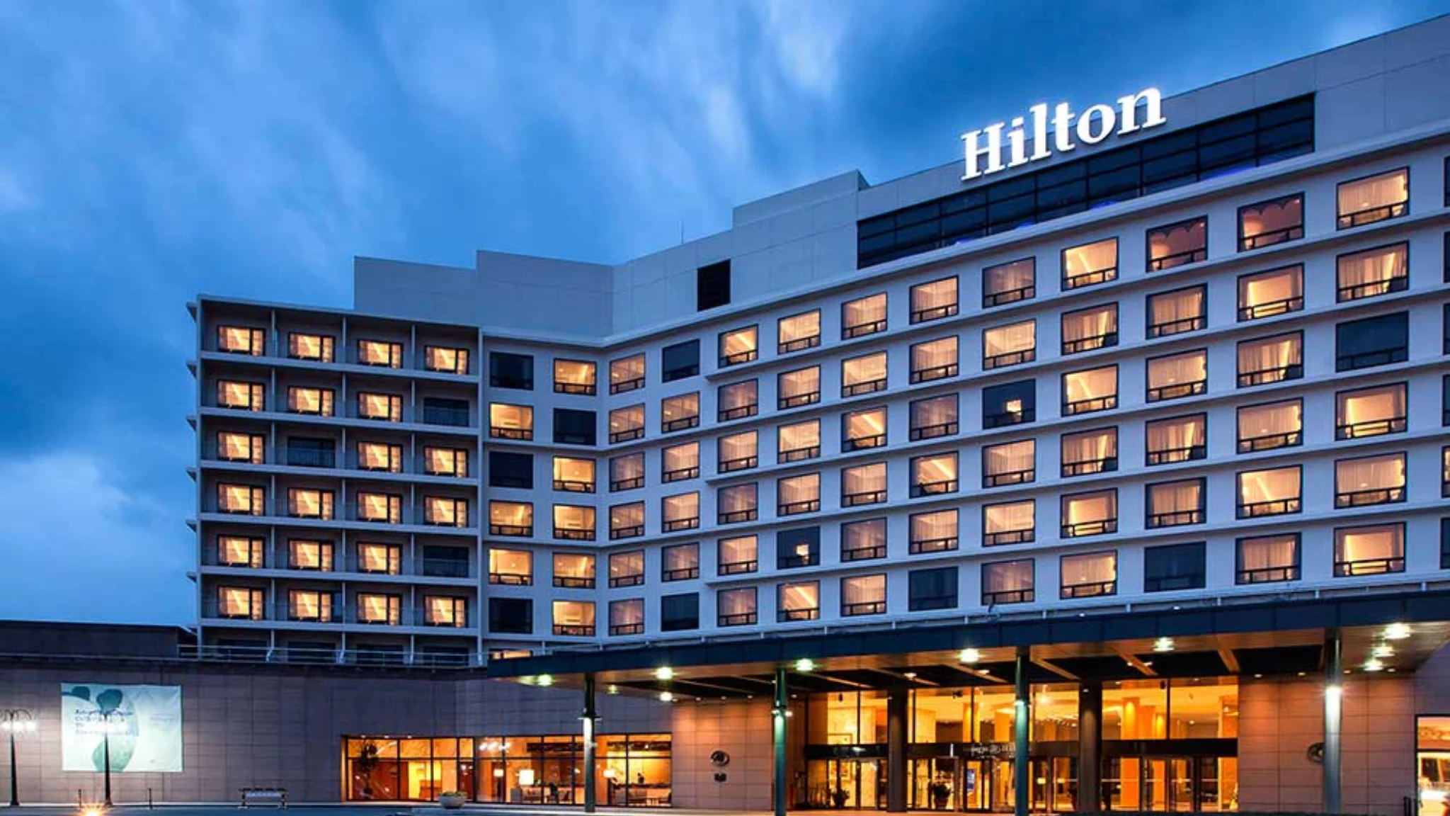 Hilton hotel illuminated at night, showcasing its elegant architecture and warm lights against the evening sky.