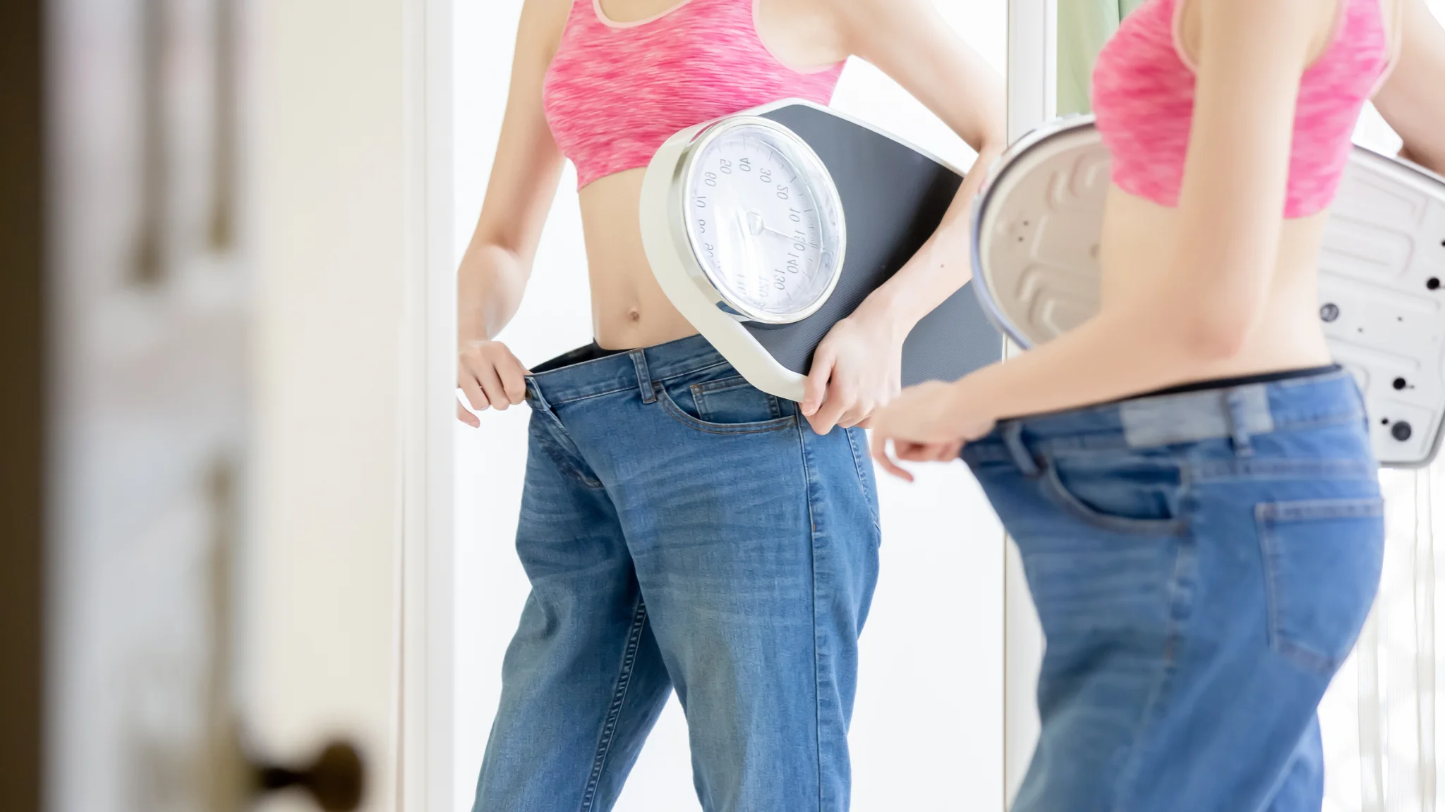 Two women dressed in jeans, each holding a scale, sharing a lighthearted moment together.