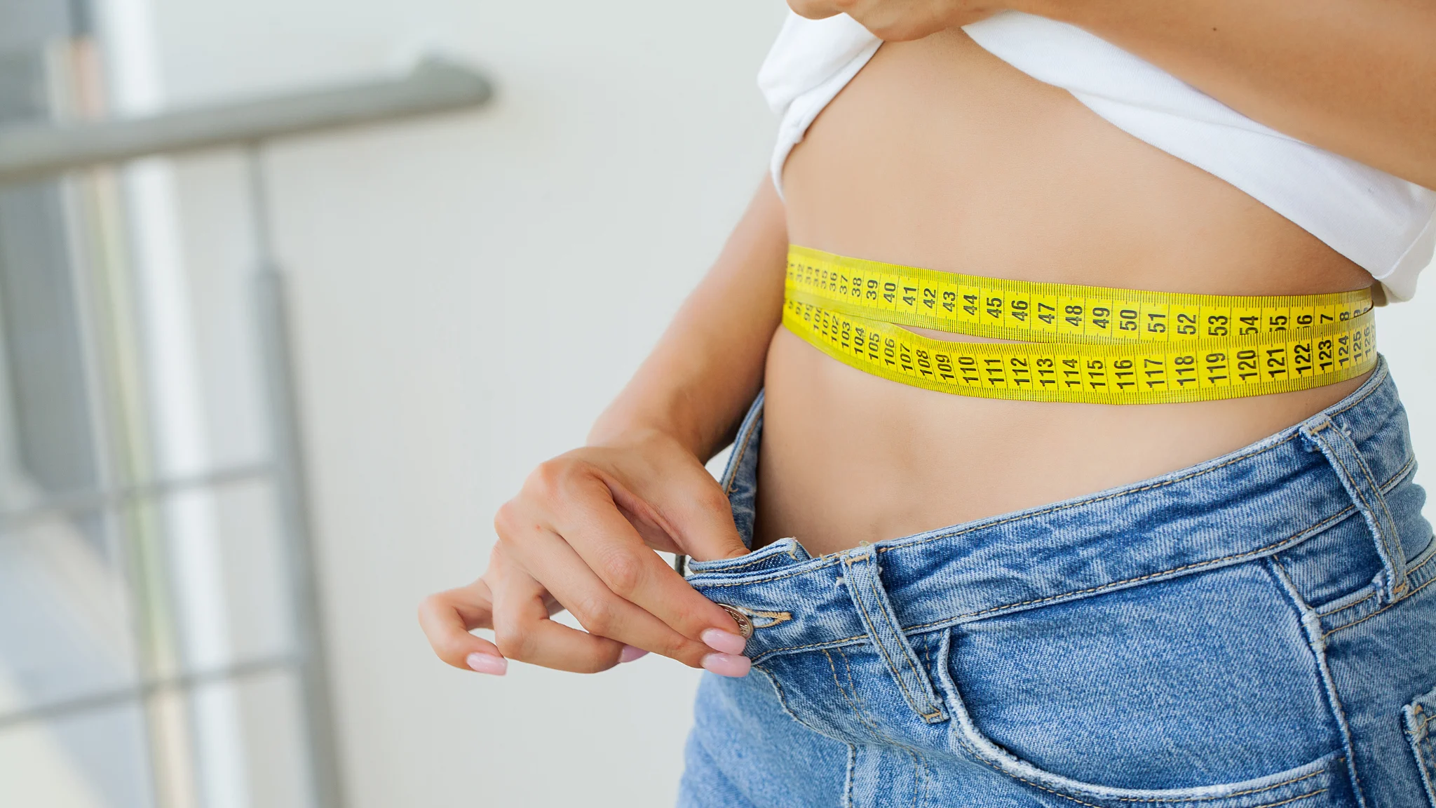 A woman measures her waist with a tape measure, focusing intently on her fitness goals.