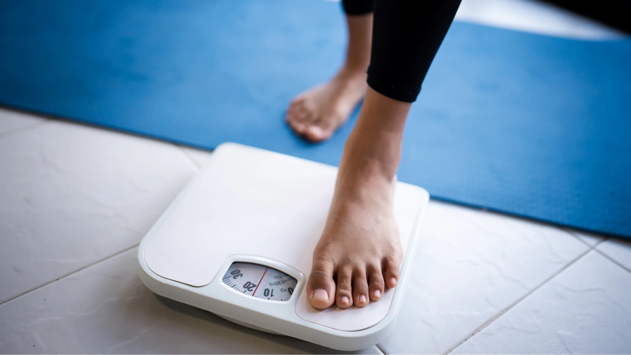 A person stands on a scale, feet firmly on the floor, checking their weight with a focused expression.