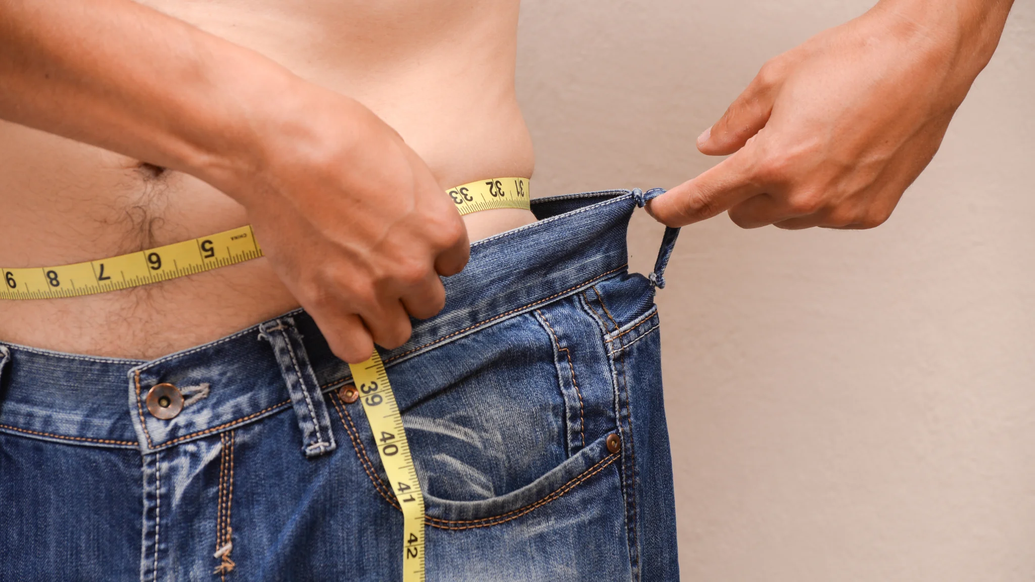 A man measures his waist with a tape measure, focusing on his fitness and health goals.