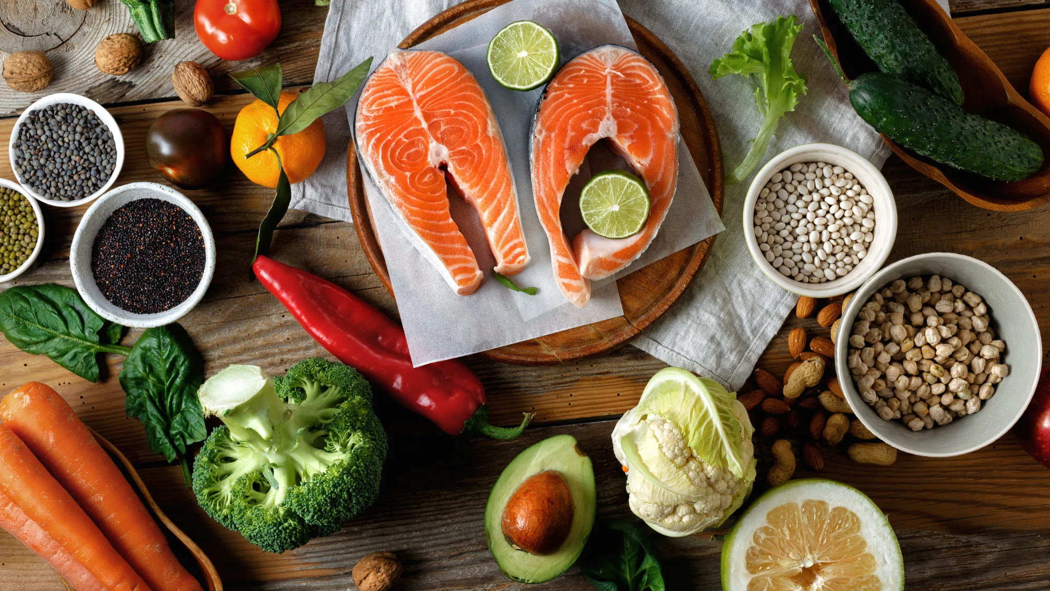 A colorful assortment of foods featuring fish, fresh vegetables, and a variety of nuts on a wooden table.