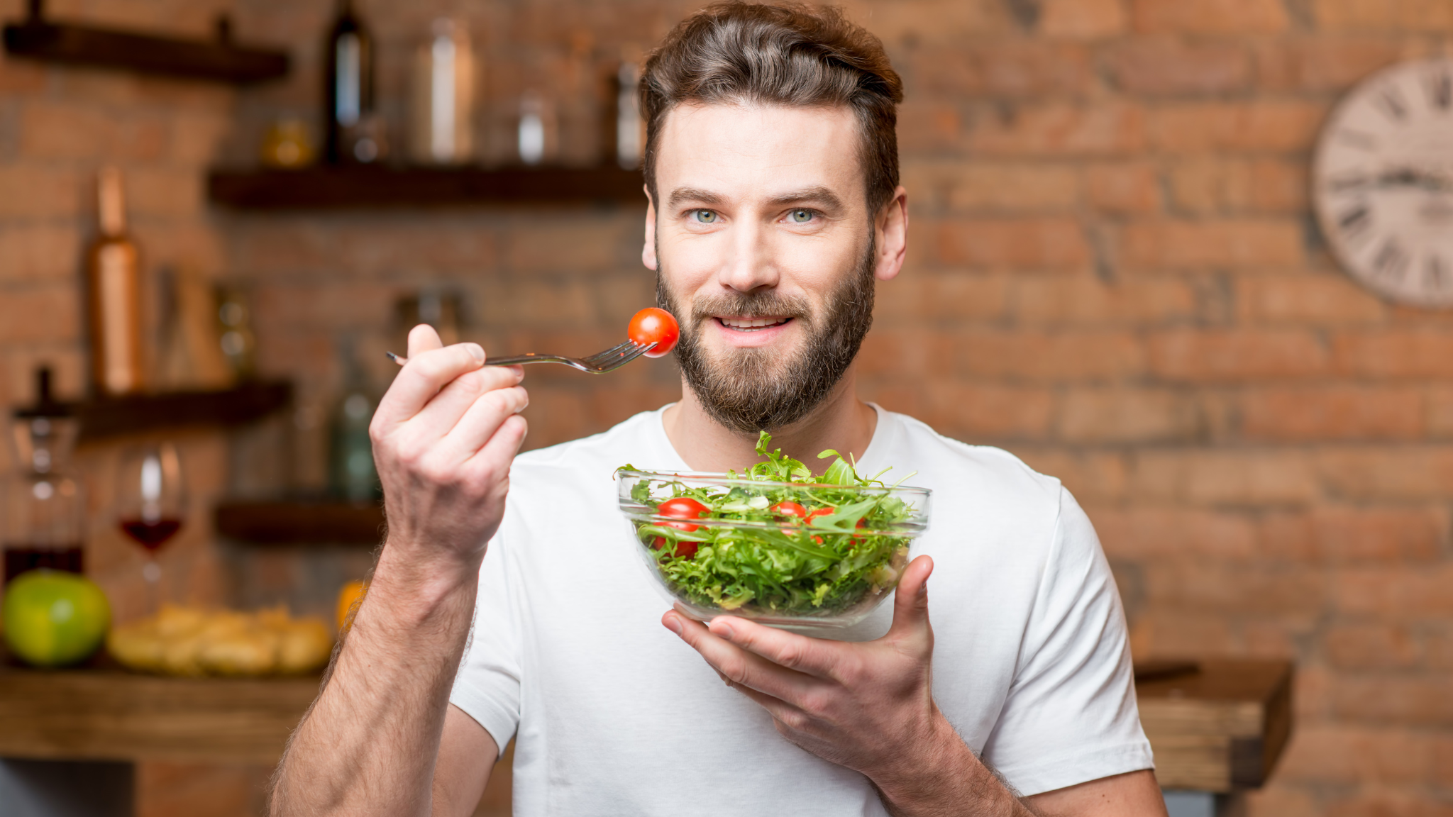 A man smiles while holding a colorful bowl of fresh salad, showcasing vibrant vegetables and greens.