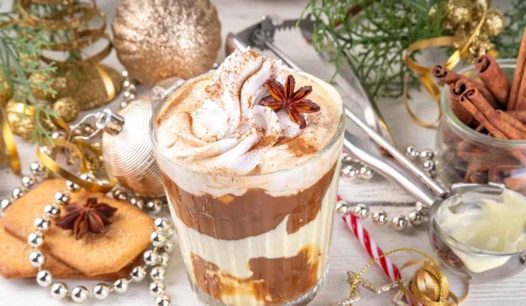 A glass of hot chocolate topped with fluffy whipped cream and a sprinkle of cinnamon.