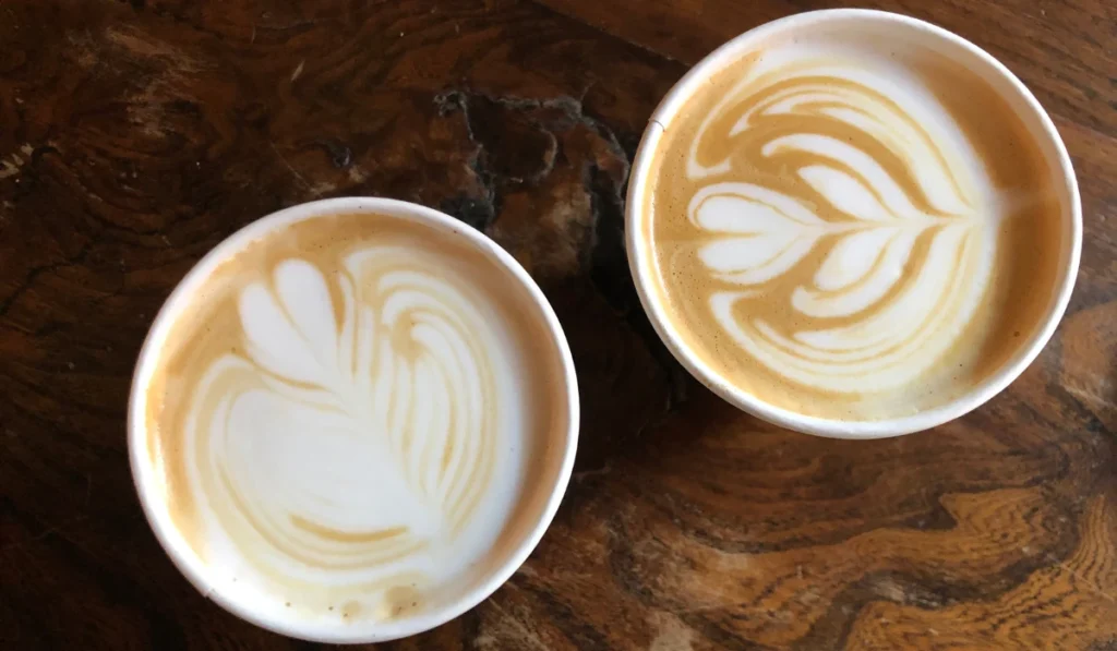 Two beautifully crafted cups of coffee with latte art rest on a warm wooden table, perfect for a relaxing moment.