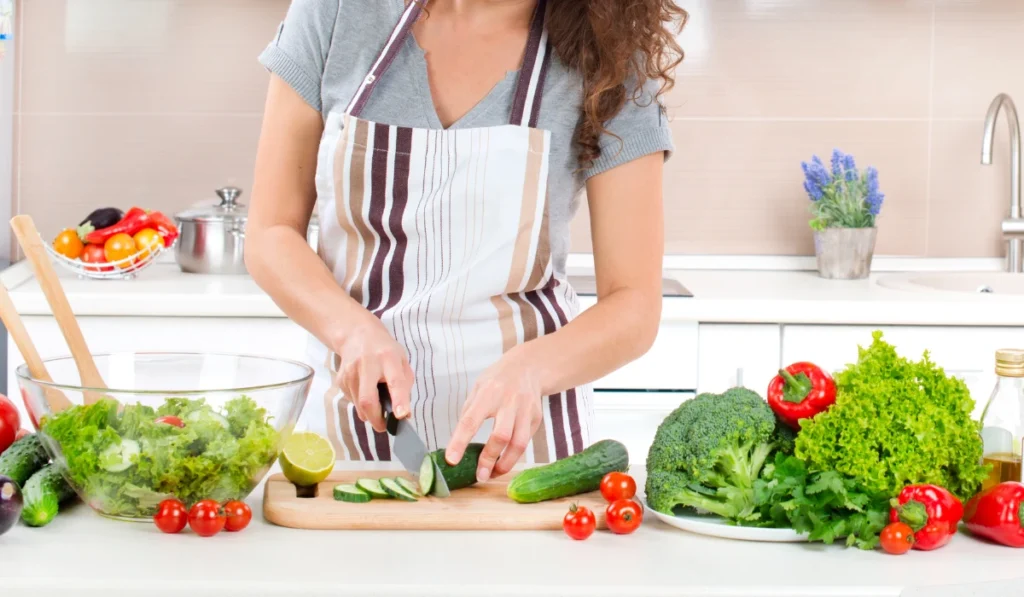 A woman chopping colorful vegetables on a cutting board in a bright kitchen.