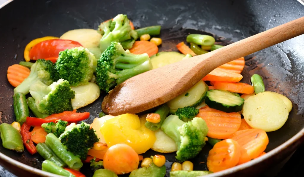 A pan filled with colorful vegetables sizzling as they cook on the stove.