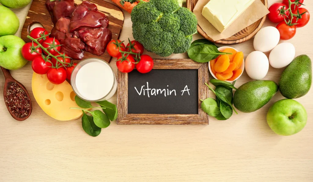 A colorful assortment of fruits and vegetables surrounds a chalkboard displaying the words "Vitamin A."