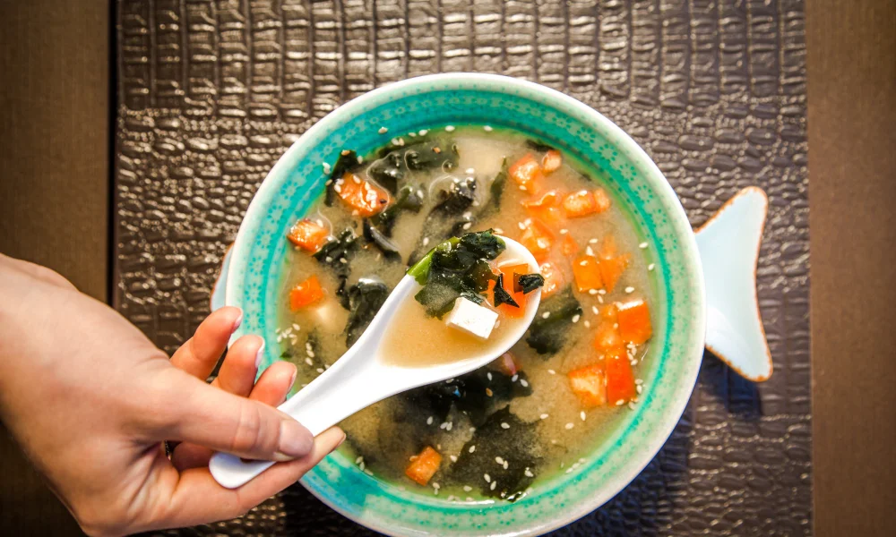 A hand holds a spoon over a blue bowl