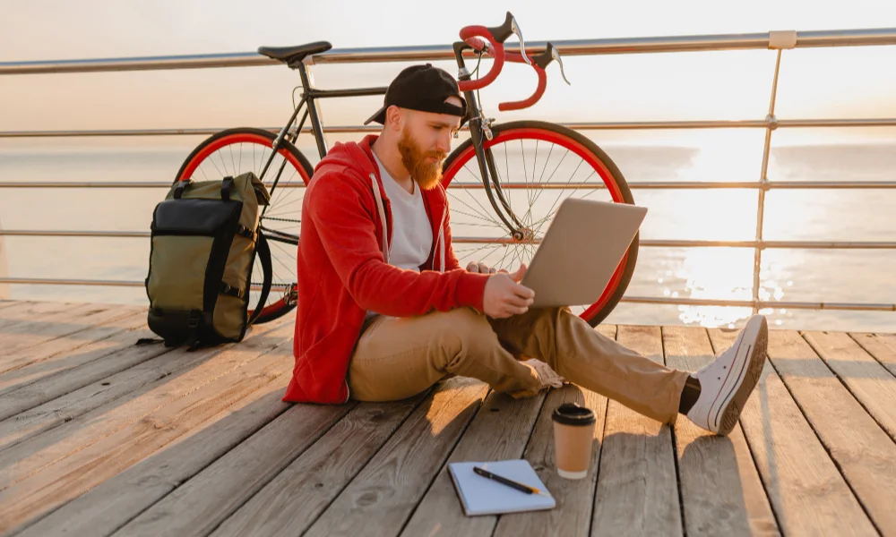 Man in a red hoodie sits on a boardwalk near a bicycle
