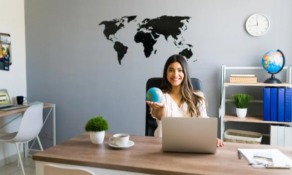 smiling woman sits at a desk holding a small globe-business travel tips