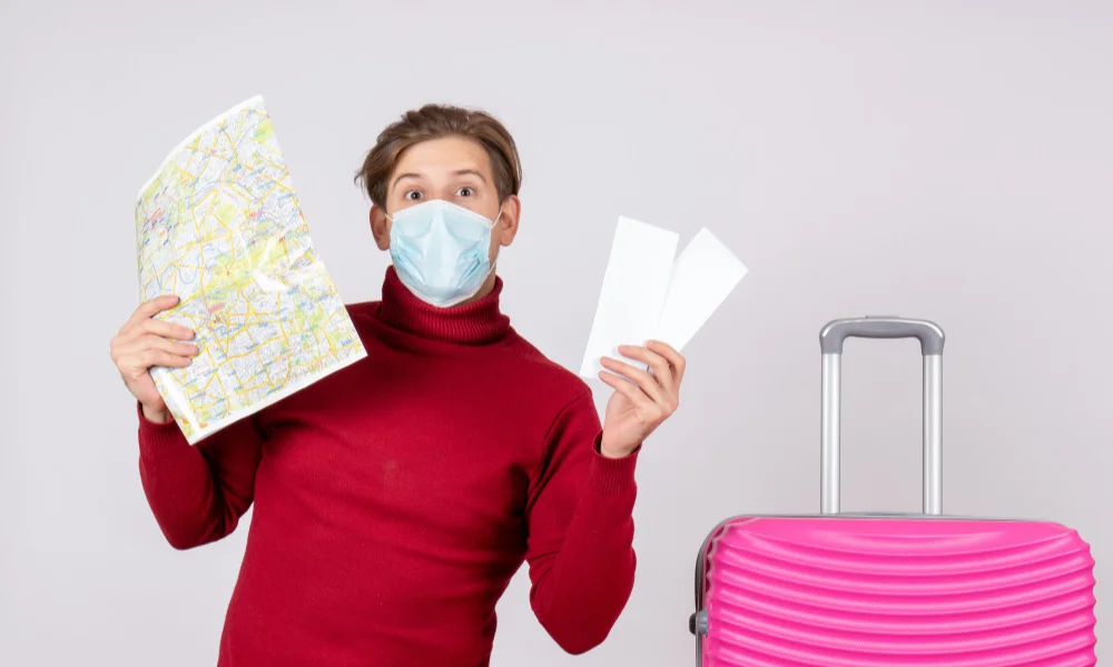 A person in a red sweater and face mask holds a map and tickets