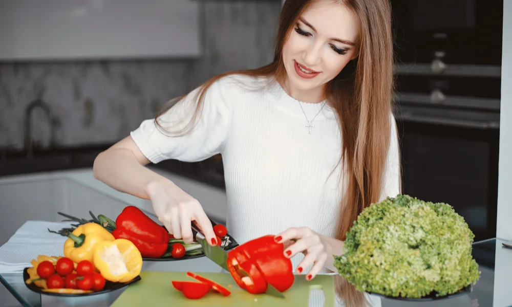 A woman in a white shirt happily slices a red bell pepper