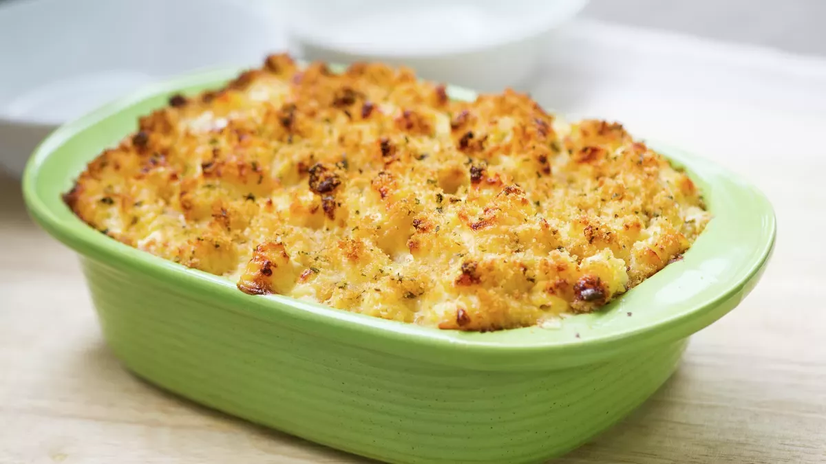 Golden-brown baked macaroni and cheese with a crispy breadcrumb topping, served in a light green oval casserole dish.