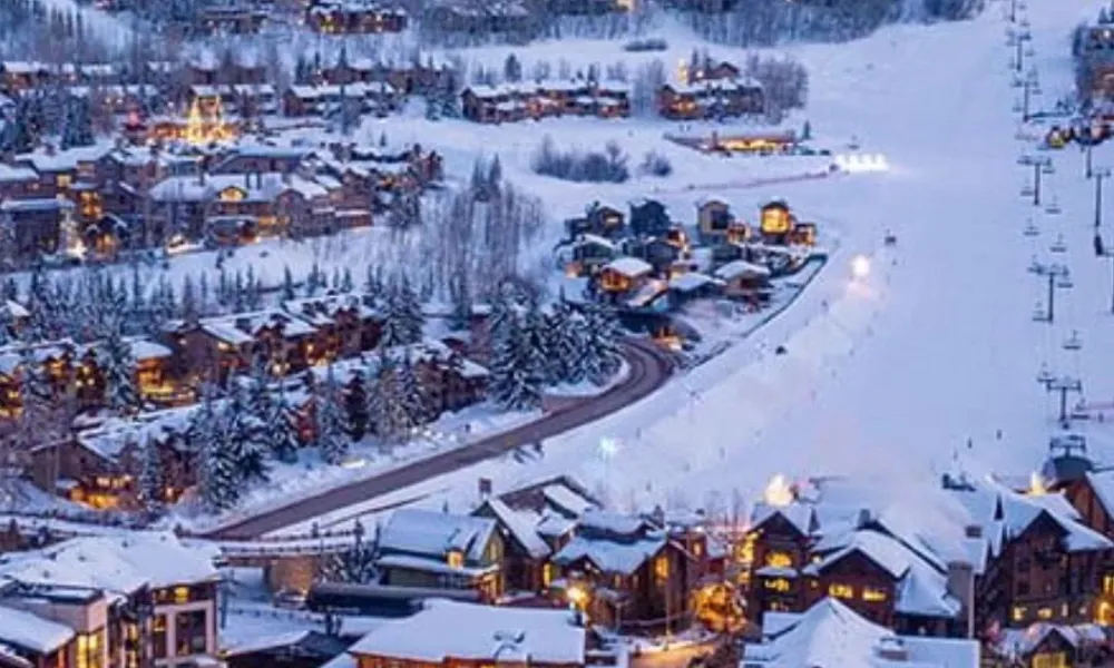 Best Ski Resorts in Colorado showcased by a twilight aerial view of luxury alpine chalets and ski trails illuminated against snowy mountain slopes in Aspen Snowmass.