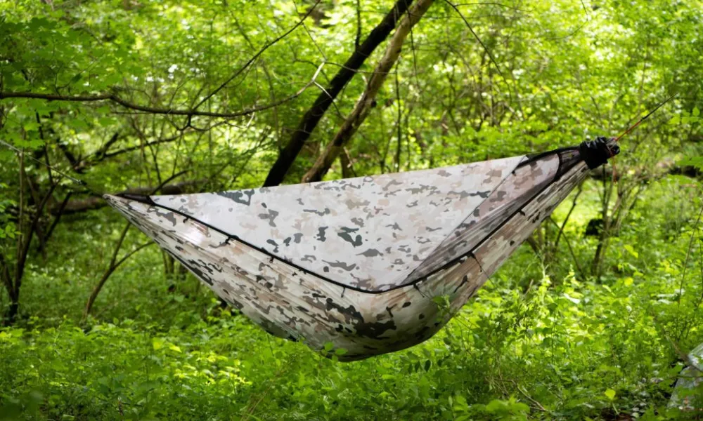 Best Camping Hammocks featuring a camouflage-patterned camping hammock with an integrated bug net suspended between trees in a lush forest.