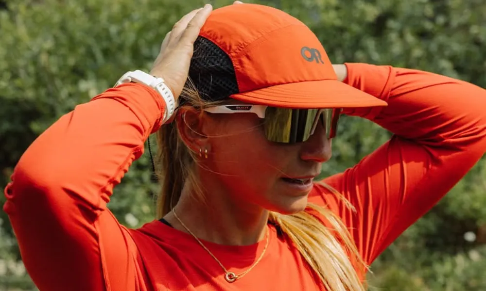 Best Hiking Hats featured in a bright orange Outdoor Research cap worn by a hiker wearing sunglasses outdoors. 