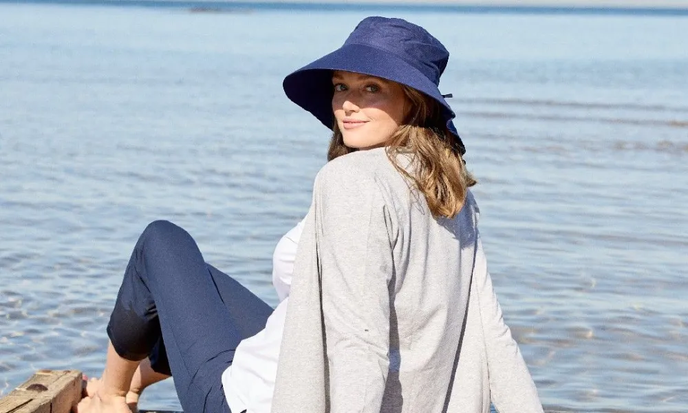 Best Hiking Hats demonstrated by a woman wearing a navy blue wide-brim UV protection sun hat while relaxing on a wooden pier by the water. 