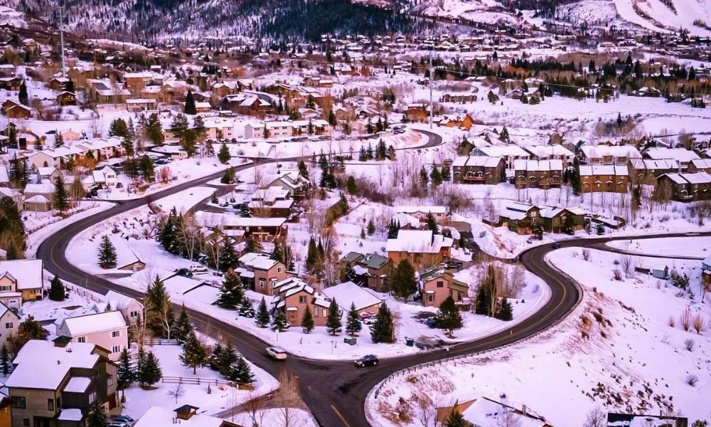 Best Ski Resorts in Colorado highlighted by a panoramic aerial view of a snow-covered mountain town and winding roads framed by dusk-lit ski slopes in Steamboat Springs.