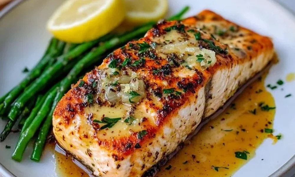 A pan-seared salmon fillet topped with melted butter and herbs, served with tender green asparagus and lemon slices, demonstrating healthy inspiration for easy Mediterranean recipes