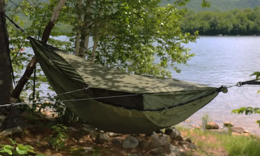 Best Camping Hammocks set up with an olive green Warbonnet Blackbird hammock with side tie-outs pitched beside a tranquil lake.