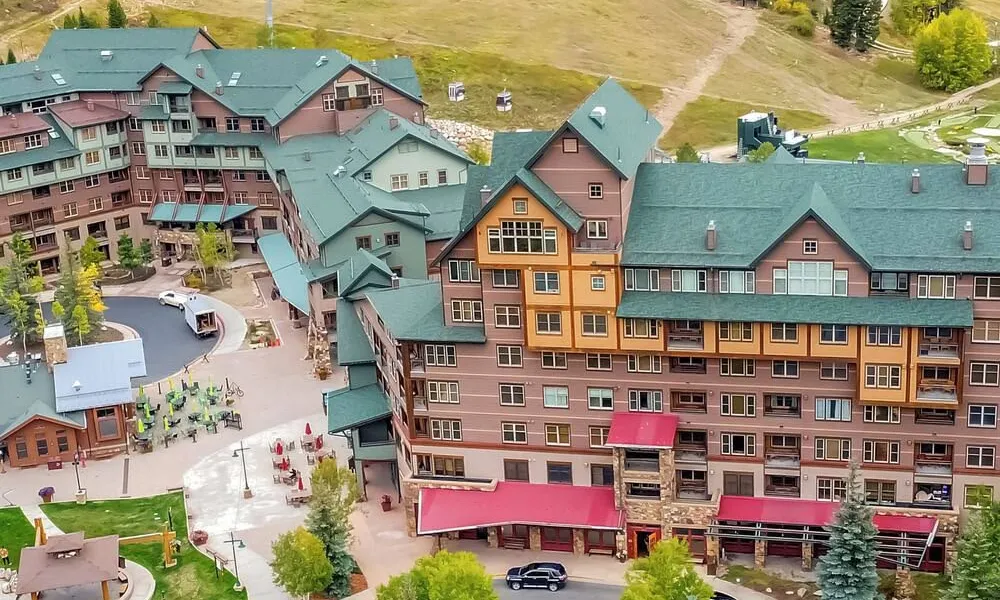 Best Ski Resorts in Colorado highlighted by an aerial view of a mountain resort lodge and village surrounded by autumn foliage and pine trees.