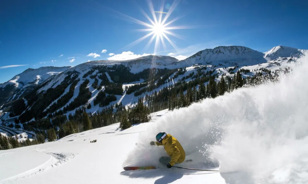 Best Ski Resorts in Colorado showcased by a skier carving through fresh powder snow beneath a brilliant sunlit mountain sky.