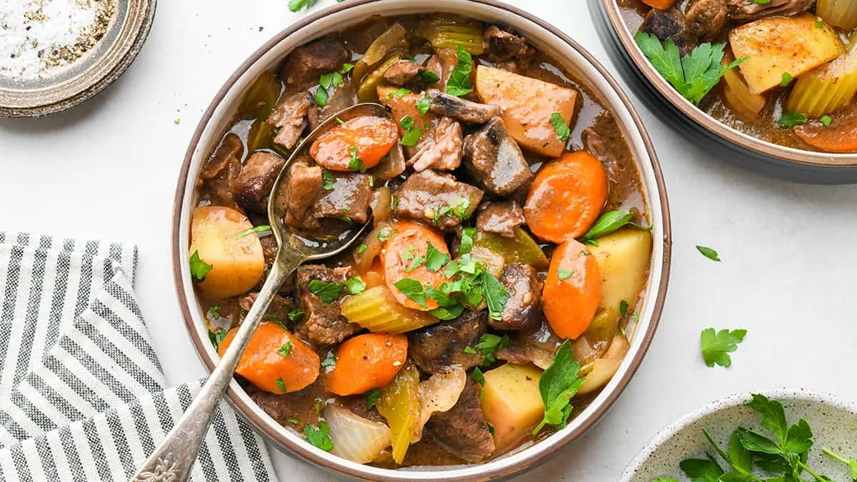 Hearty beef stew filled with tender beef chunks, potatoes, sliced carrots, and celery in a rich gravy, garnished with fresh parsley and served in a bowl with a spoon.