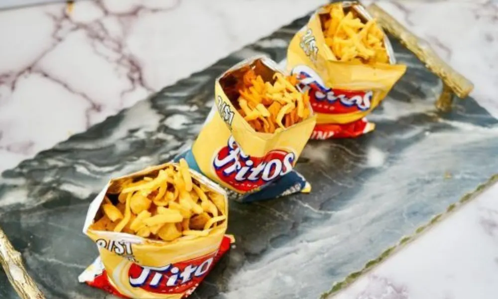 Three individual Fritos chip bags filled with chili and shredded cheese, creating a walking frito pie.